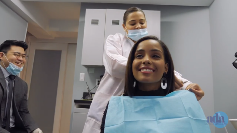 woman in a dentist ' s chair getting her teeth brushed by a man