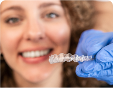 smiling woman holding a clear plastic retainer in her hand