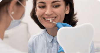 woman in blue shirt brushing teeth with blue gloves while another woman in white shirt looks on