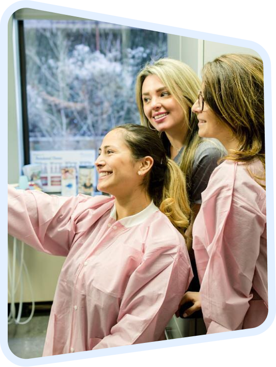 three women in pink coats are looking at a computer screen